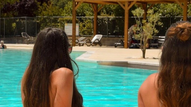 Zwei Personen sitzen am Pool, im Hintergrund eine Holzpergola und Liegestühle.