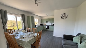 A dining area with a table set for four, wooden chairs, and a view of the kitchen in the background. - Christinas Cottage - Family- Garden-wifi-sleeps 6 (Downpatrick)