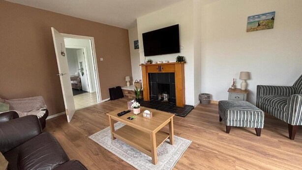 A living room with a fireplace, a television mounted above it, and striped ottomans. - Christinas Cottage - Family- Garden-wifi-sleeps 6 (Downpatrick)
