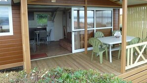 Un espace extérieur abrité, doté d’une table et de chaises, une porte-fenêtre coulissante donnant sur une cuisine et une vue sur l’extérieur.