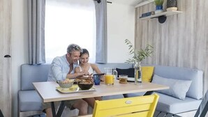 A dining area with a table, chairs, and a sofa. There are plants on a shelf above the sofa. - ZEcamping 4* 200m plage piscine couverte pet friendly tente TV LV 31m2 (Plomodiern)