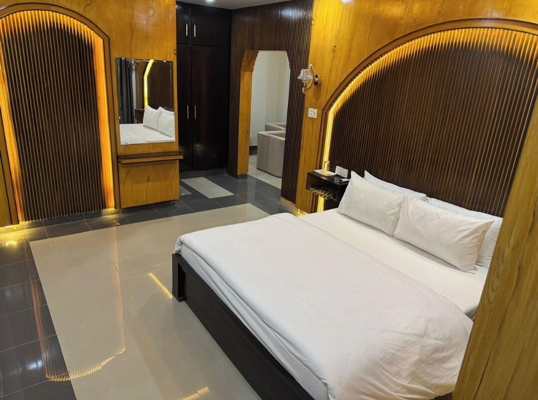 A hotel room with a large bed, wooden headboard, a nightstand, and a mirror.