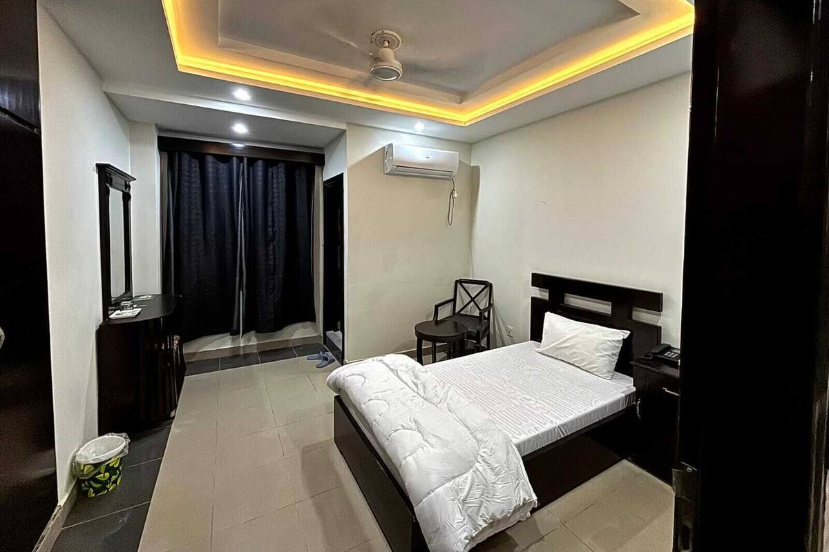 A hotel room with a bed, bedside table, chair, and a small desk with a chair.