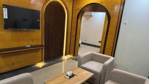 A modern room with a flat-screen TV mounted on a wooden wall, a wooden coffee table, and two grey sofas. - Sapphire Stays Peshawar  (Peshawar)