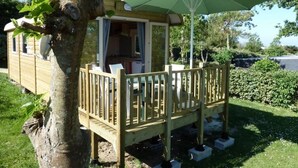 A wooden deck with a covered seating area, a large umbrella, and a view of a house with a window and a satellite dish.