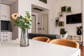 En moderne stue med en hvid sofa, en glasvase med blomster, et fladskærms-tv og indbyggede reoler med planter.