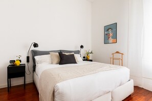 Un dormitorio ordenado con cama, mesitas de noche, un sillón colgante y una obra de arte en la pared.