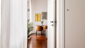 A hallway with a white door, a potted plant, a table with chairs, and two framed pictures on the wall. - Garibaldi - Modern 1 BR in Brera by Rentopolis (Milan)
