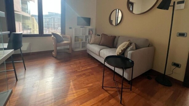 Una sala de estar moderna con piso de madera, un sofá blanco, una silla negra y un espejo redondo en la pared.