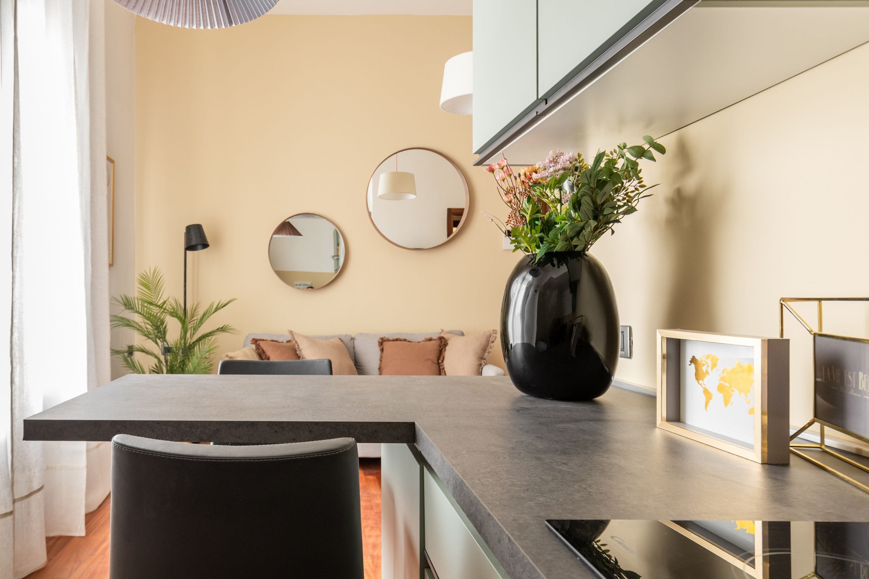 A modern kitchen with a dining table, chairs, a vase with flowers, and a world map framed picture.