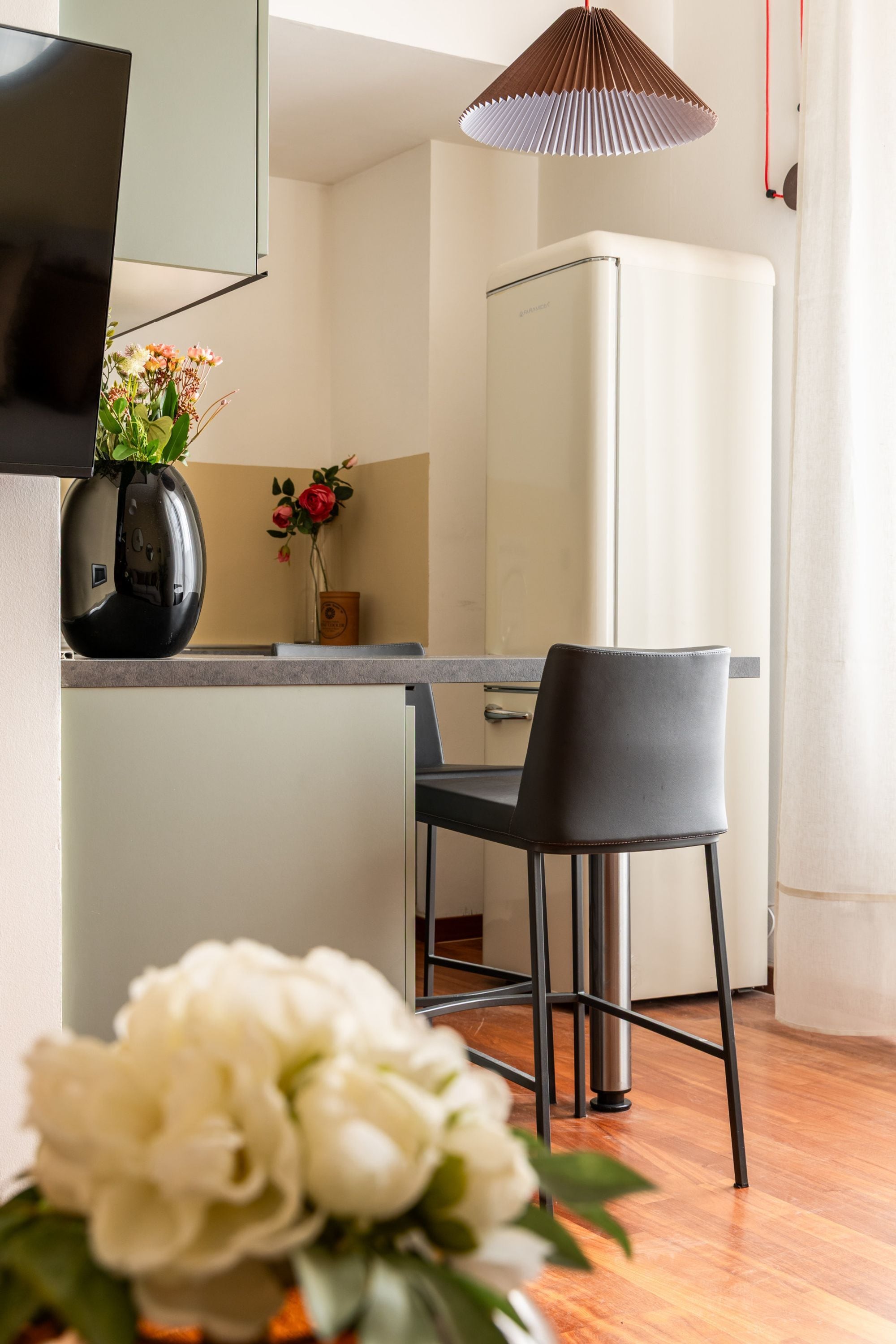 Una cucina moderna con un frigorifero bianco, una sedia nera e un vaso con fiori sul piano di lavoro.