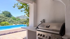 Ein Grillbereich im Freien mit Blick auf einen Swimmingpool und Bäume.