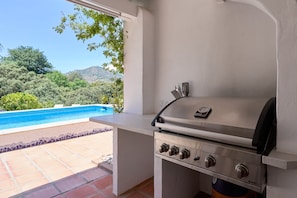 Un área de parrilla al aire libre con vista a una piscina y árboles.