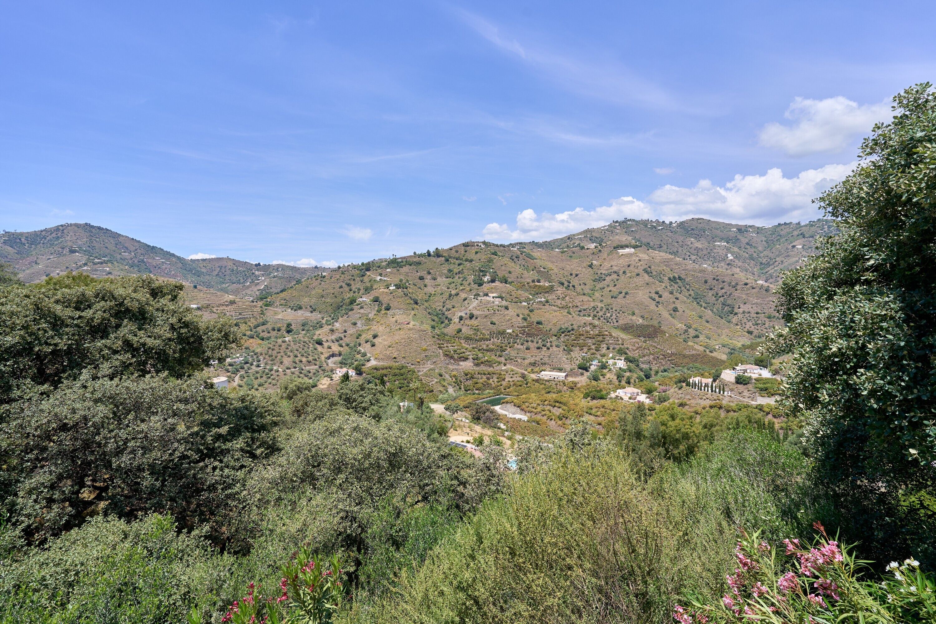 A mountainous landscape with scattered buildings, dense vegetation, and a clear sky.