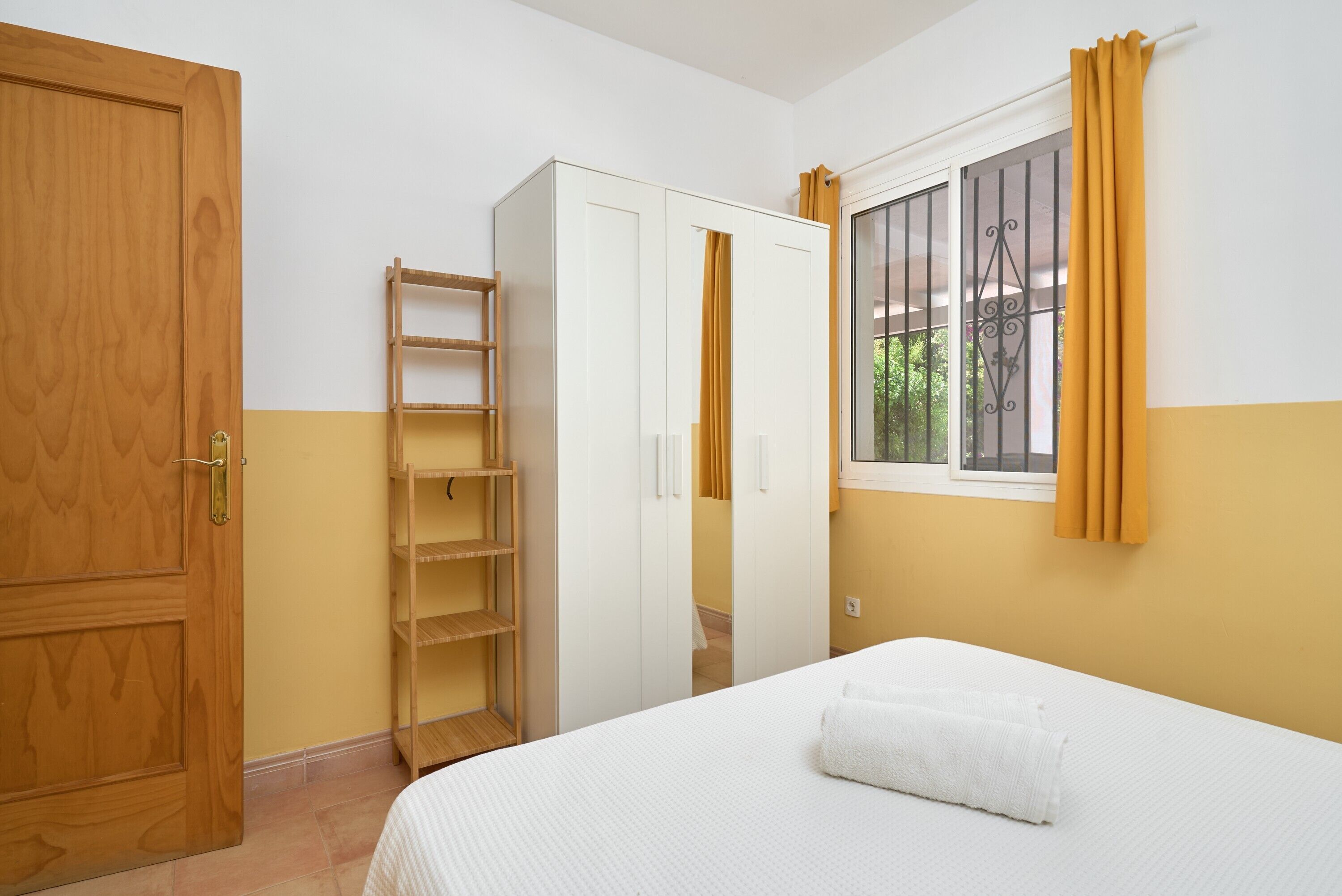 A bedroom with a bed, wardrobe, and window with curtains.