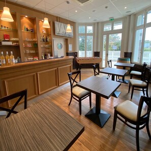 A restaurant with wooden tables and chairs, a bar area with shelves of bottles, and large windows allowing natural light. - ZEcamping animaux acceptés à 5mn à pied des plages (Saint-Malo)