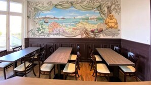 Un ristorante con un murale raffigurante un paesaggio tranquillo e una statua del Buddha seduto. Tavoli e sedie disposti per la ristorazione.