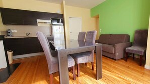 Un espacio habitable compacto con una mesa de comedor, dos sillas, un sofá y una cocina con armarios oscuros y un refrigerador.
