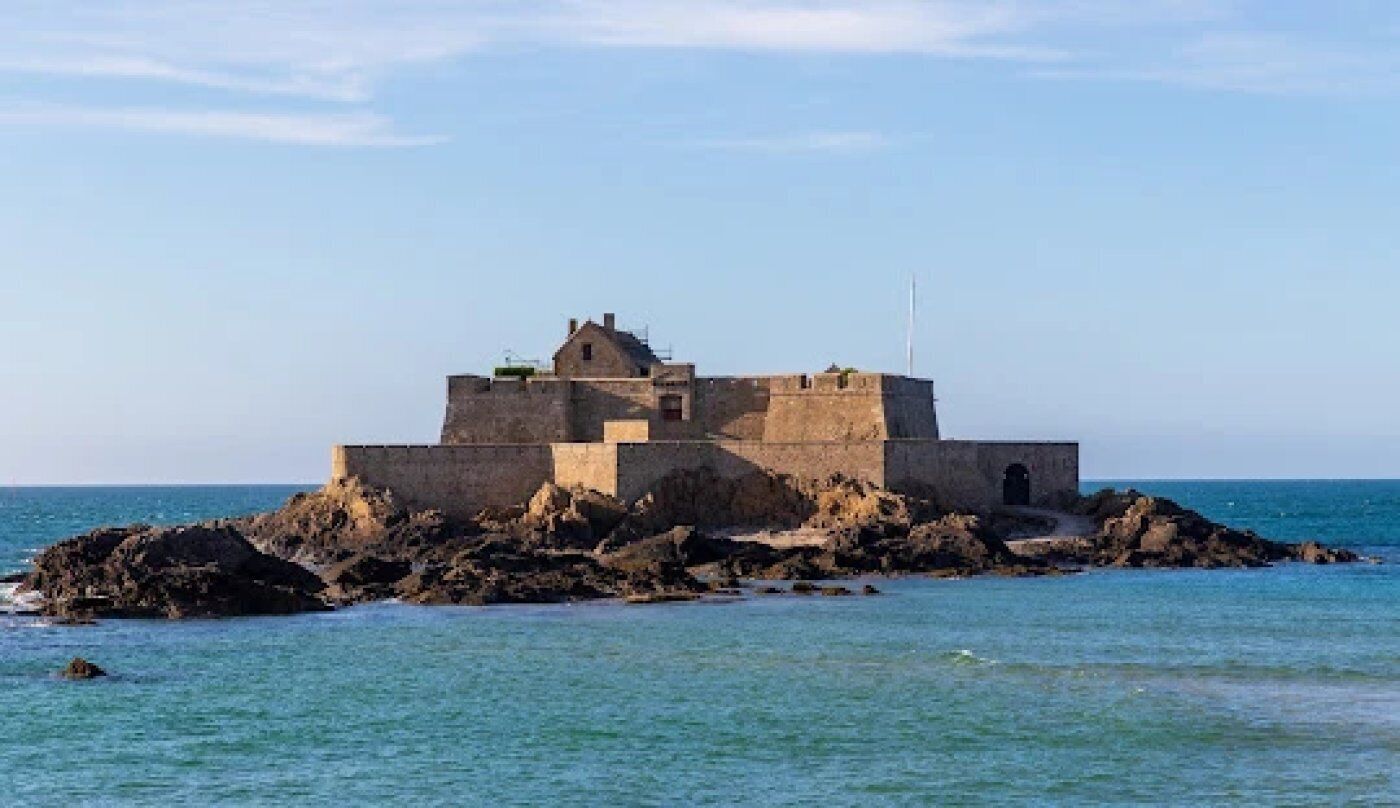 Una fortificazione costiera con una torre centrale e un’antenna, circondata da un terreno roccioso e dal mare.