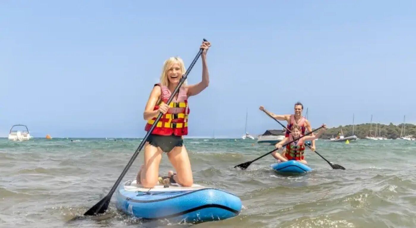 Zwei Personen paddeln auf einem ruhigen Meer, im Hintergrund sind Boote zu sehen.