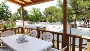 A covered outdoor area with a table and chairs, overlooking a residential neighborhood with houses and trees. - ZEcamping 3* 200m plage locatif TV clim 28m2 6 pers (Hyères)
