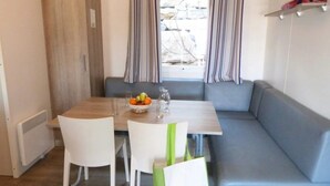 A dining area with a table, chairs, and a bench. There is a bowl of fruit on the table. - ZEcamping 3* 200m plage locatif TV clim 28m2 6 pers (Hyères)