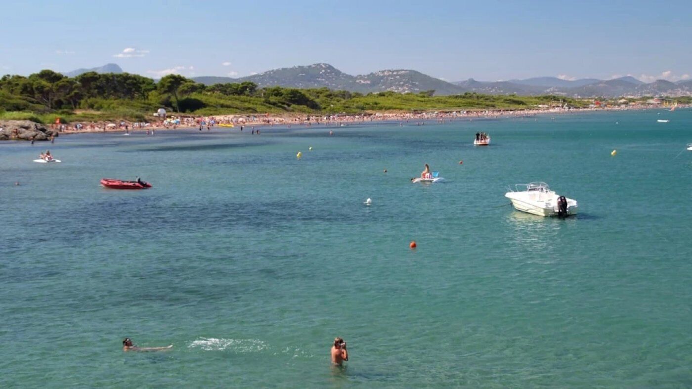 Un paysage côtier avec des bateaux, des baigneurs et une plage.