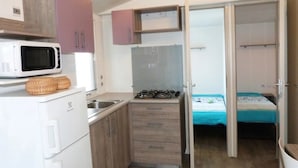 A compact kitchenette with a microwave, sink, and stove, and a bedroom with a bed and a window. - ZEcamping 3* 200m plage locatif TV clim 28m2 6 pers (Hyères)