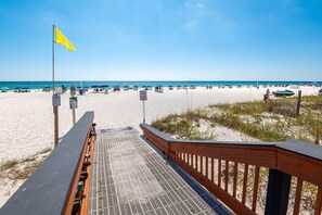 A beach with a wooden walkway leading to the sand, a yellow flag, and beach umbrellas. - 1704 Seawind w Free Umbrella Svc Double Balcony (Gulf Shores)