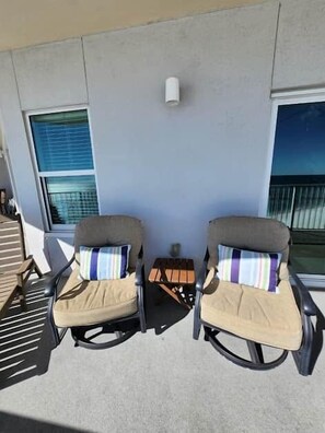 Two outdoor chairs with cushions, a small table, and a wall-mounted light fixture. - 1704 Seawind w Free Umbrella Svc Double Balcony (Gulf Shores)