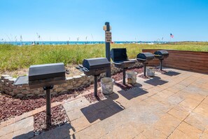 An outdoor grill area with a caution sign, a stone wall, and a view of the beach. - 1704 Seawind w Free Umbrella Svc Double Balcony (Gulf Shores)