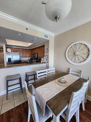 A dining area with a table, chairs, and a decorative wall piece. - 1704 Seawind w Free Umbrella Svc Double Balcony (Gulf Shores)
