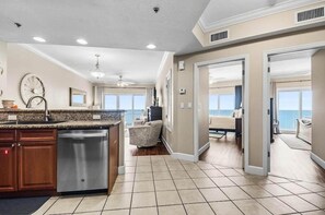 A spacious kitchen with a dishwasher, a dining area with a chair, and a view of the ocean through large windows. - 1704 Seawind w Free Umbrella Svc Double Balcony (Gulf Shores)