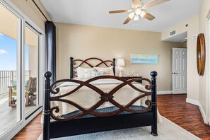 A bedroom with a bed, a ceiling fan, a view through a sliding door, and a door leading to another room. - 1704 Seawind w Free Umbrella Svc Double Balcony (Gulf Shores)