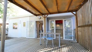 En overdækket terrasse med et bord og stole, en skydedør samt et træhegn.
