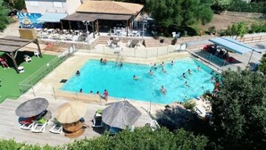 En swimmingpool med mennesker, liggestole og parasoller.