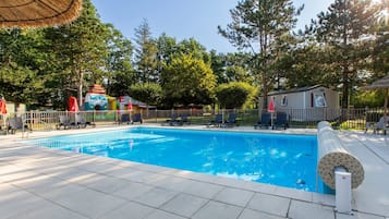 Une piscine avec des chaises longues et un parasol en chaume.