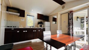 Une cuisine moderne avec des meubles de couleur sombre, un four à micro-ondes et une machine à café. On y trouve également un coin repas avec une table en bois et des chaises rouges.