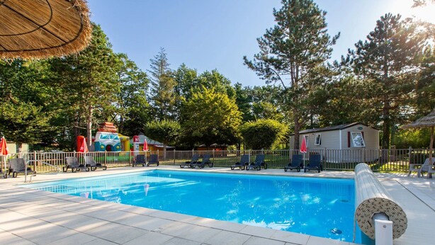 Une piscine avec des chaises longues et un parasol en chaume.