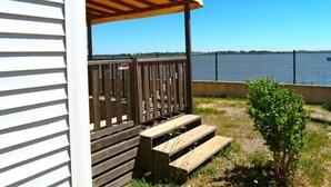 A wooden deck with a pergola, a small bush, and a view of a body of water. - ZEcamping 4* piscine chauffée pet friendly mobil-home TV BBQ clim 31m2 (Portiragnes)