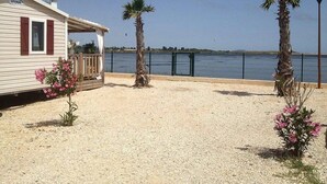 A beachfront property with a covered deck, palm trees, and a view of the sea. - ZEcamping 4* piscine chauffée pet friendly mobil-home TV BBQ clim 31m2 (Portiragnes)