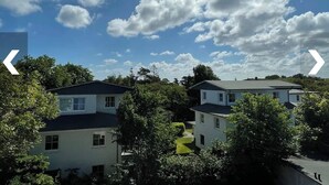 Ein Wohngebiet mit zweigeschossigen Häusern, umgeben von Bäumen und einem klaren Himmel mit Wolken.