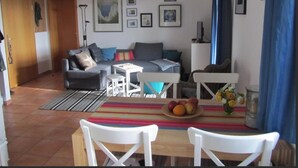 Ein Wohnzimmer mit Sofa, Couchtisch und Sesseln, ein Essbereich mit Tisch und Stühlen sowie eine Küchenzeile mit Herd und Spüle.