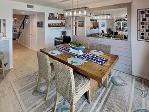 A dining area with a wooden table, woven chairs, and a central island with a bowl and plant. - Allegro North #406 | Bayfront Condo w/Great Views & Private Balcony (Rockport)