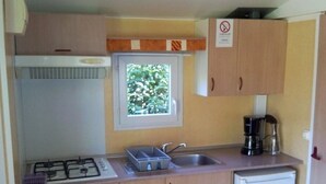 A compact kitchen with a gas stove, sink, and a small refrigerator. - ZEcamping 3*chiens acceptés piscine en bord de rivière avec Canoë (Mazères)