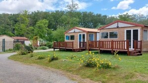 A row of wooden mobile homes with attached porches, surrounded by a grassy area and trees.