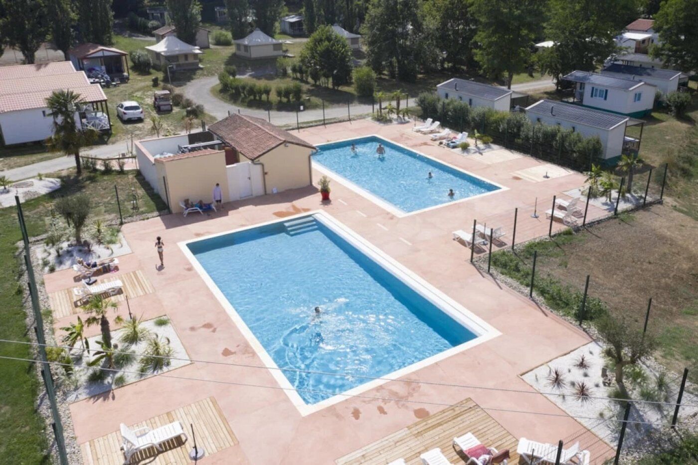 Et boligområde med to rektangulære swimmingpools, omgivet af liggestole og palmer.