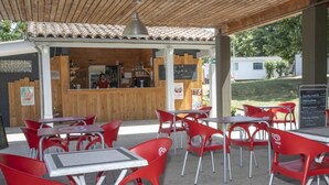 An outdoor café with red chairs and tables, a wooden counter with a chalkboard menu, and a view of a residential area.