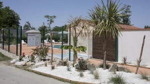 A fenced outdoor area with a pool, palm trees, and a small building with a tiled roof.