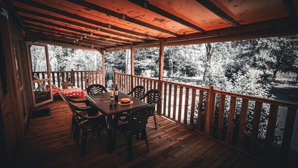 Une terrasse en bois avec une table et des chaises, donnant sur une zone boisée.